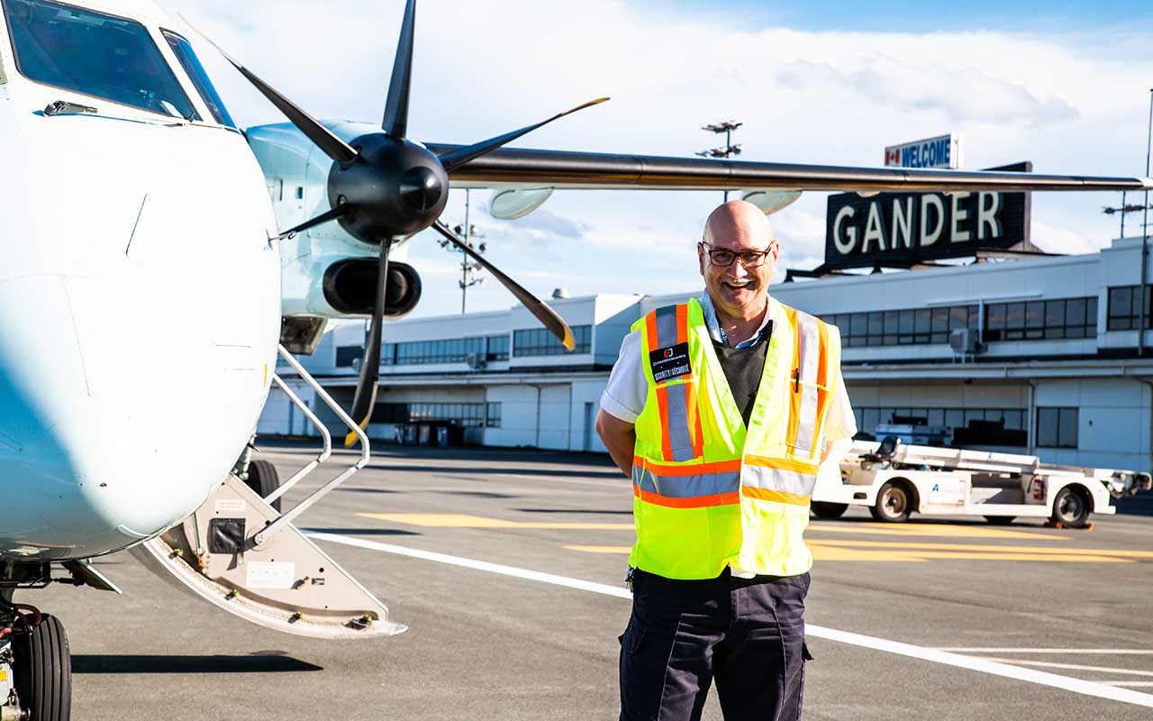 Contemporary Gander International Airport photograph of a staff member beside an aircraft beneath the terminal's visible “WELCOME GANDER” sign.